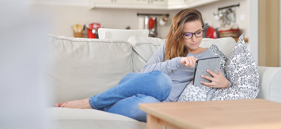 A teenager sits on the couch using a tablet.